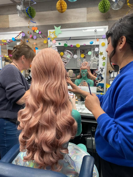 Elle Fanning sits in the makeup chair as wig stylist Celeste Gonzalez adjusts her pink wig.